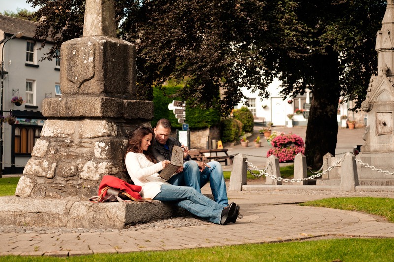 A couple sits on the stone base of the 17th-century Fitzgerald Monument in the tree-lined village square of Inistioge, County Kilkenny, looking at a map together.