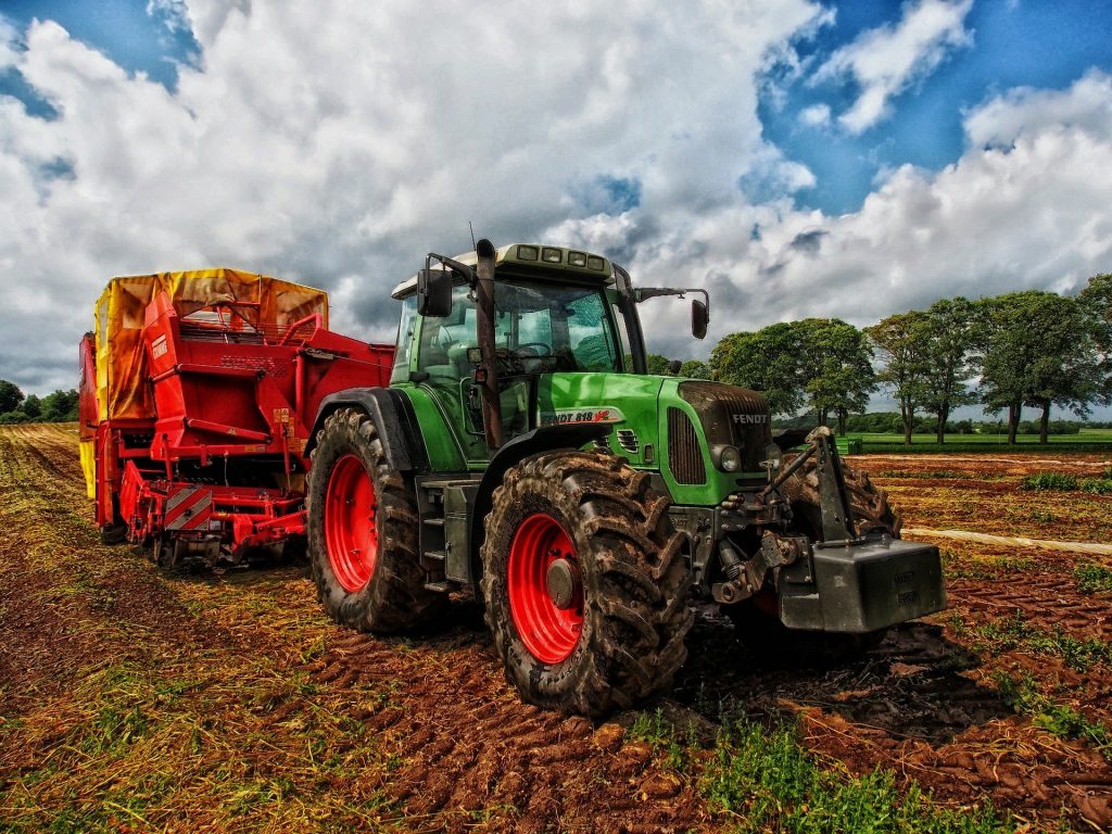 A green Fendt tractor with red wheels pulls a red potato harvester through a muddy field under a dramatic, cloudy sky.