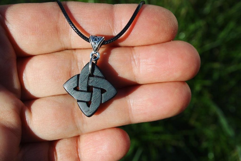 A hand holding a Celtic knot necklace.