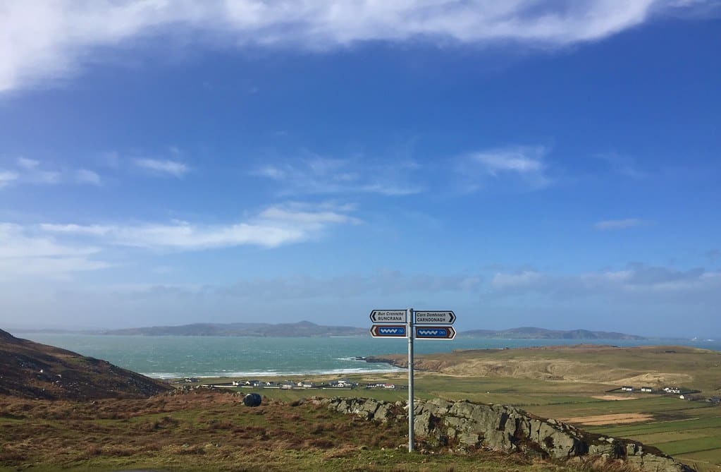 A sign pointing out the Wild Atlantic Way with rolling hills and water in the distance.