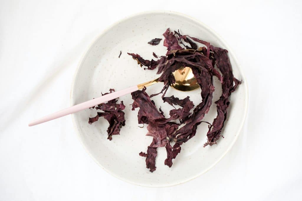 Dried purple dulse seaweed strips arranged on a white plate and gold spoon.