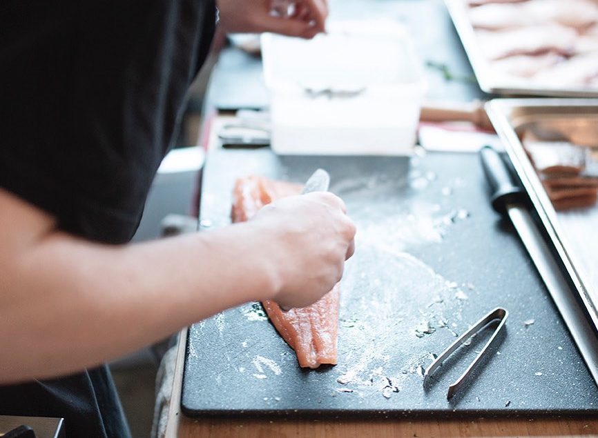 A chef at Roam restaurant in Belfast, one of Belfast's must-visit foodie destinations, skillfully prepares a salmon dish, showcasing the culinary expertise and vibrant dining scene of the city.