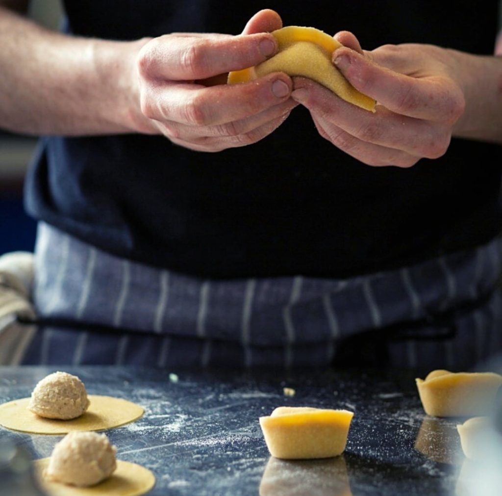 A chef expertly prepares tortellini pasta, delicately folding the dough around savory filling, showcasing culinary skill and precision in the art of pasta-making.