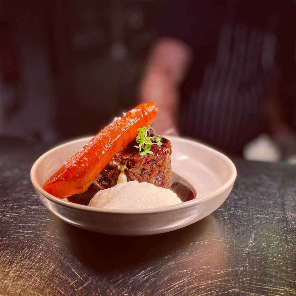 A beautifully plated dish featuring slices of beef feather blade served with creamed celeriac, showcasing a gourmet meal with vibrant colors and elegant presentation.