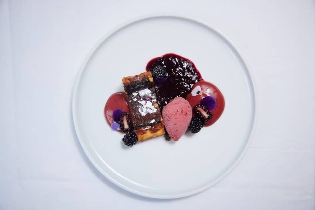 A delectable Burnt Basque Cheesecake topped with ripe and plump blackberries, showcasing its rich texture and vibrant fruit accents.