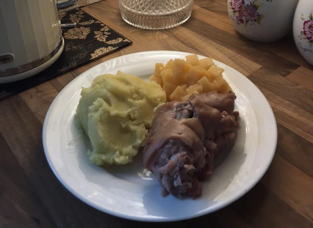 A white plate served with traditional boiled crubeens (pork trotters) alongside generous scoops of mashed potatoes and turnip.