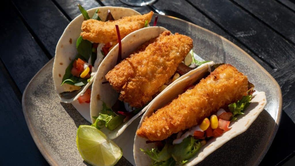 Three seafood tacos next to each other on a plate with a piece of lime.