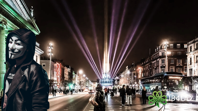 A composite image of the Dublin night scene featuring a person in a Guy Fawkes mask and hoodie in the foreground with an "IB4UD" logo in the corner.