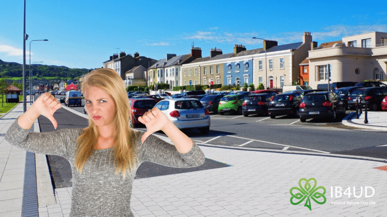 A woman giving a double thumbs-down gesture in front of the seafront and colourful buildings in Bray, County Wicklow