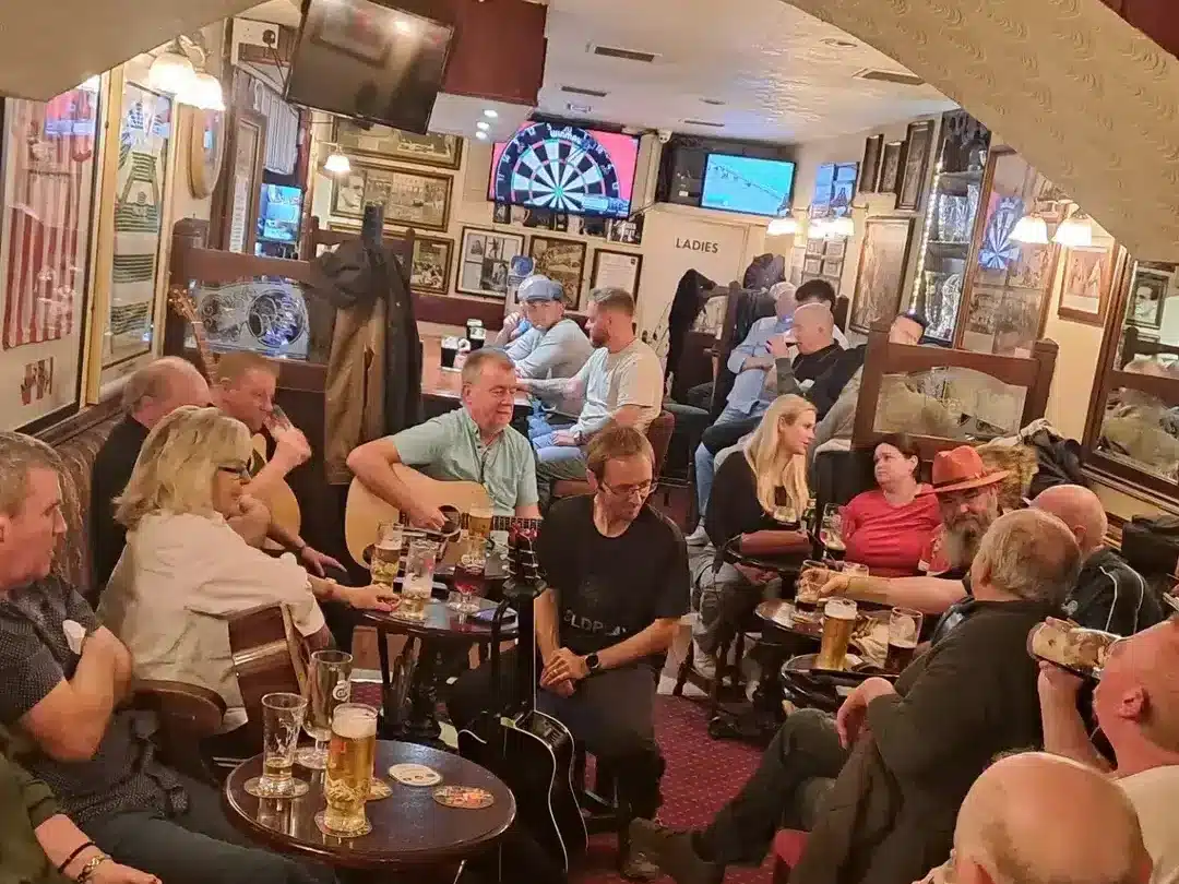 The Harold House is busy with people playing music, drinking pints, with darts on TV in the background.