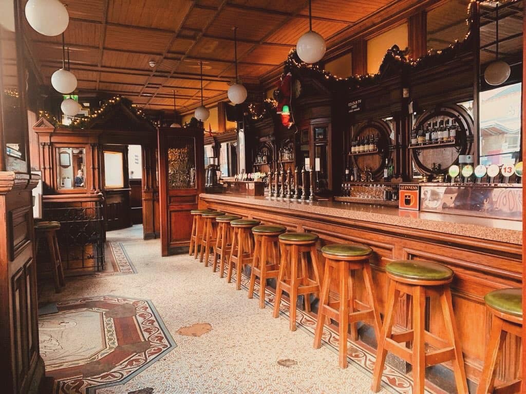The Swan bar sits empty. A brightly lit old, wooden clad bar with empty stools and no one on the bar.