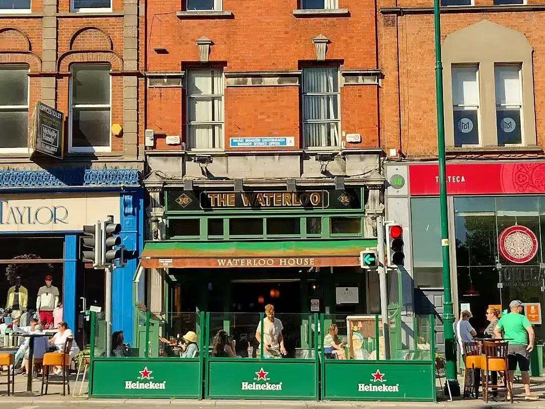 The front of The Waterloo bar in Dublin on a sunny day with people sitting outside and on the street.