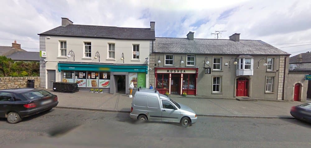 A street-view of M. O'Shea traditional pub and grocery shop, featuring classic storefronts with red and teal accents on a main road in Borris-in-Ossory, County Laois.