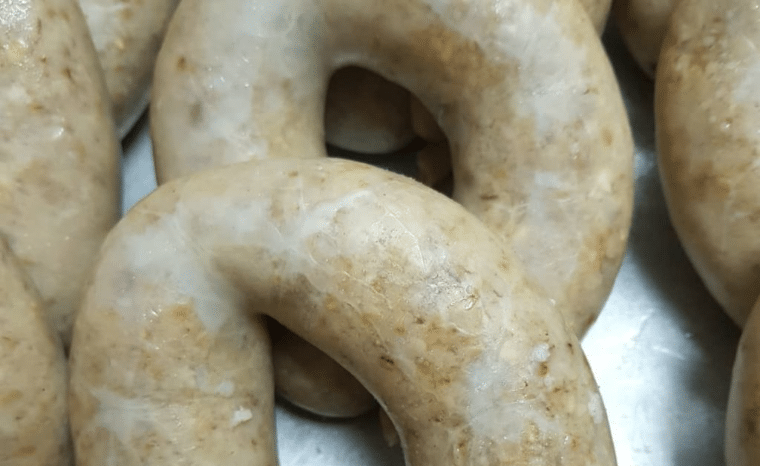 A close-up view of several curved links of traditional Irish white pudding, displaying their characteristic pale, speckled texture filled with grains and oats.