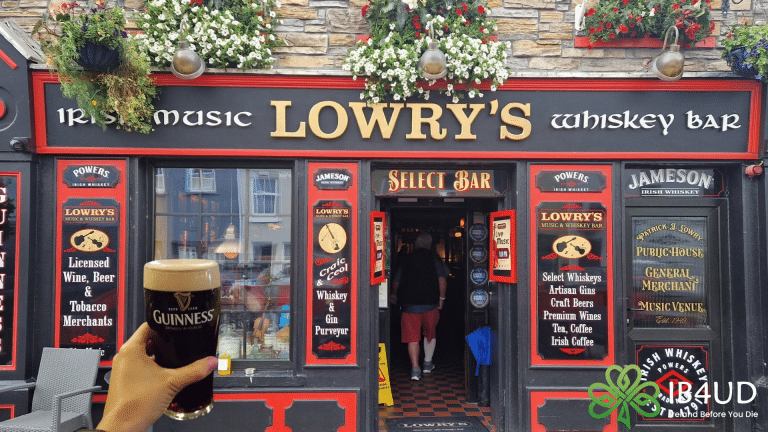 A featured image of a hand holding a fresh pint of Guinness in front of Lowry's Music and Whiskey Bar storefront.