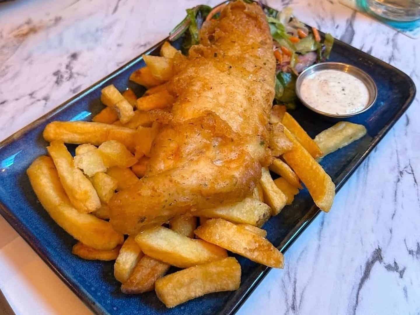 A plate of fish and chips with a side salad and a sauce.