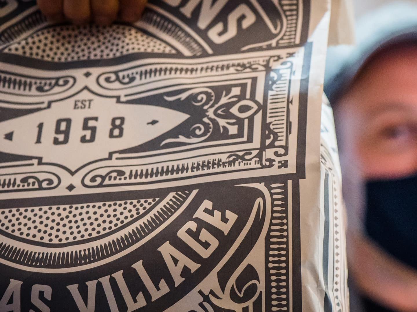 A paper bag from KC & Sons with an employee in the background holding the bag.