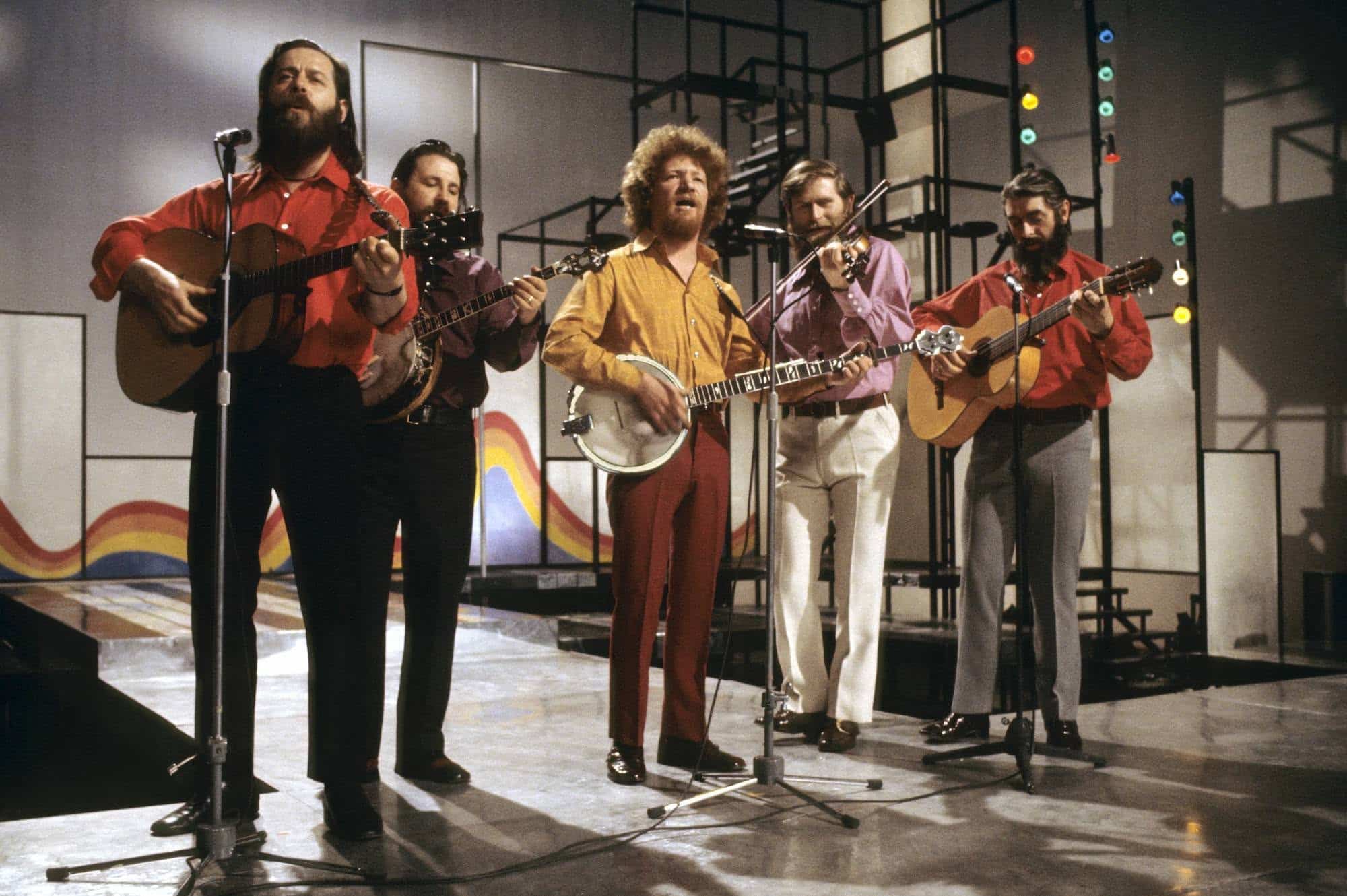The Irish folk band The Dubliners performing on a stage set playing guitars, banjos, and a fiddle.
