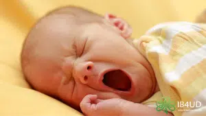 Small baby lying down yawning wearing yellow and white stripes.